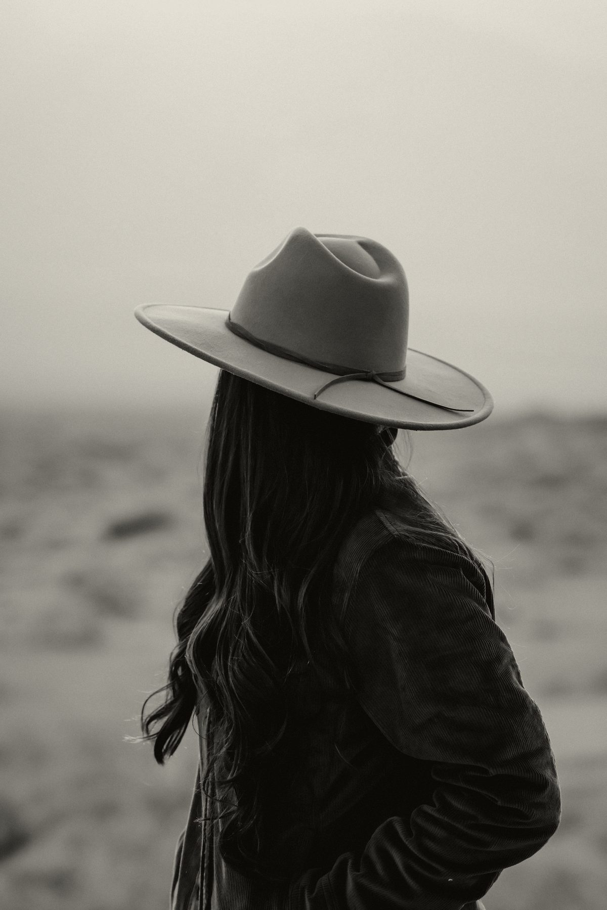 Woman in a corduroy jacket and wide-brim felt hat looking out over the desert