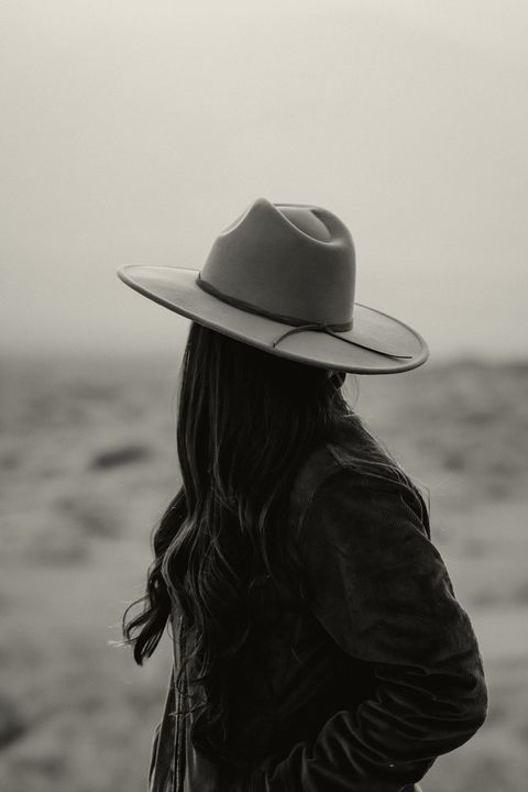 Woman in a corduroy jacket and wide-brim felt hat looking out over the desert